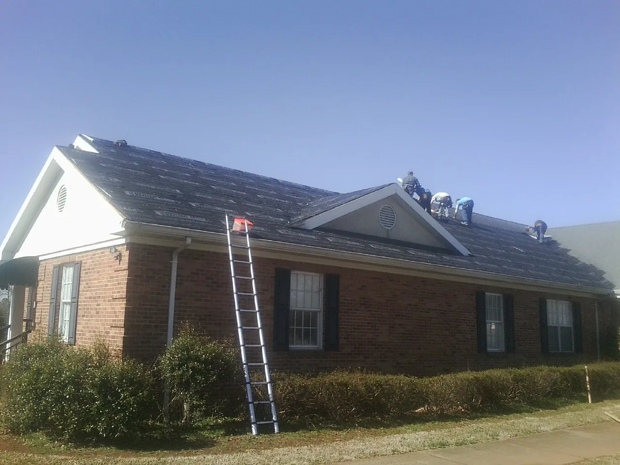 Crew tearing shingles off a brick ranch roof with a ladder set — Emergency Roof Repair work by our crew in Hillsdale