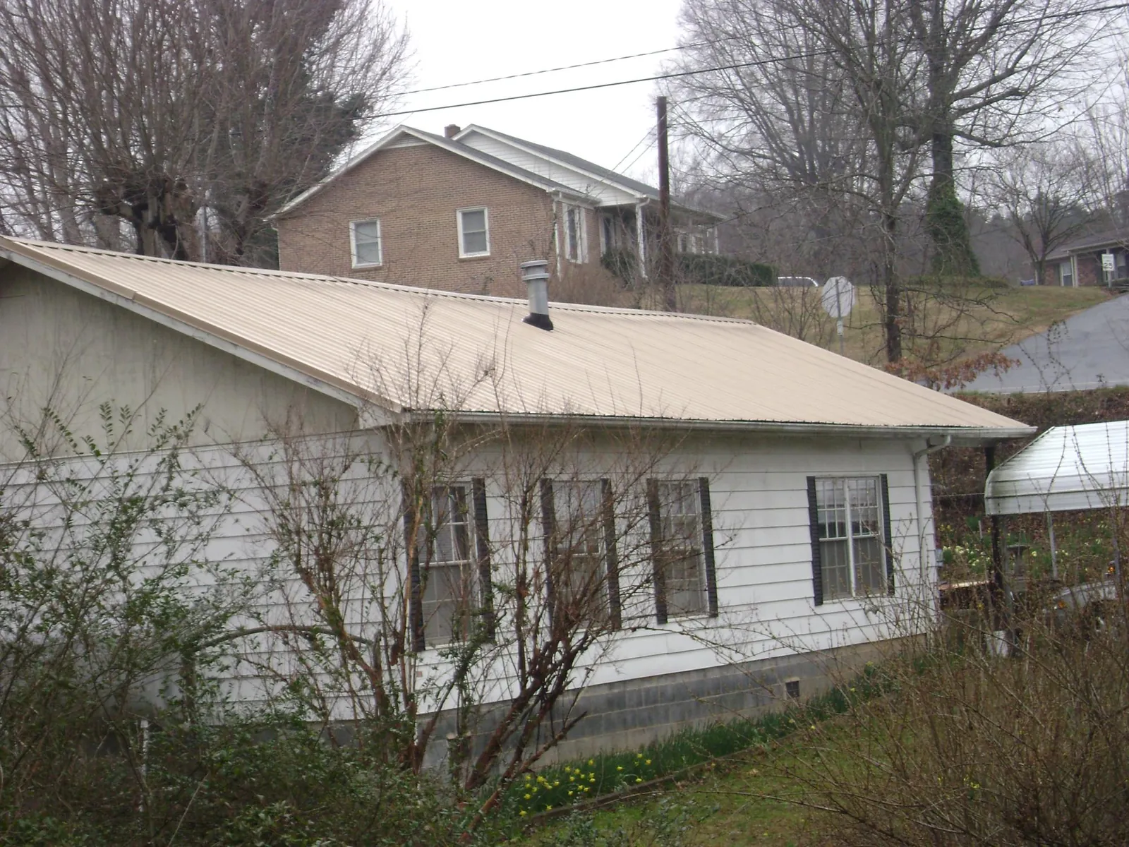 Tan metal roof on a white sided house set into a hillside — Commercial Roofing by Roofing Brothers in Hillsdale
