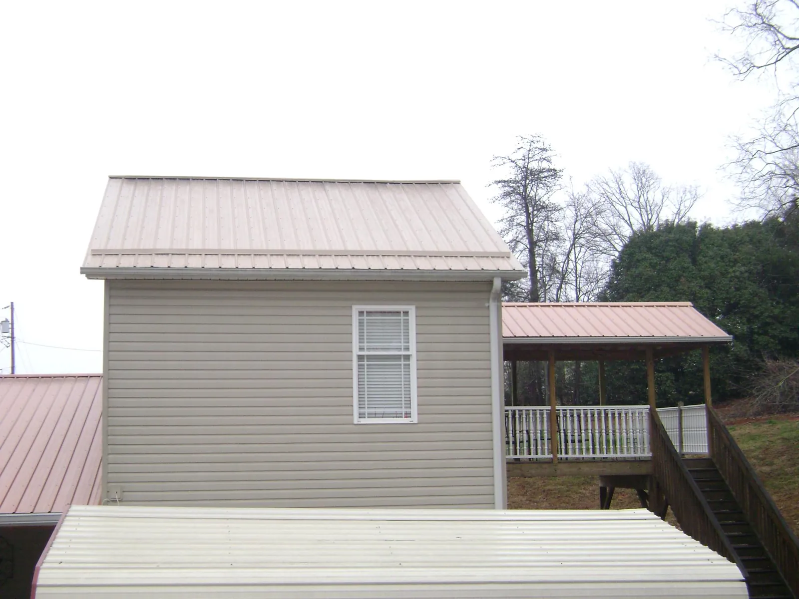 Tan metal roofs on a two story addition and attached porch, from a Roof Replacement job in Hillsdale